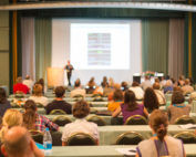 Business and entrepreneurship symposium. Speaker giving a talk at business meeting. Audience in the conference hall. Rear view of unrecognized participant in audience.